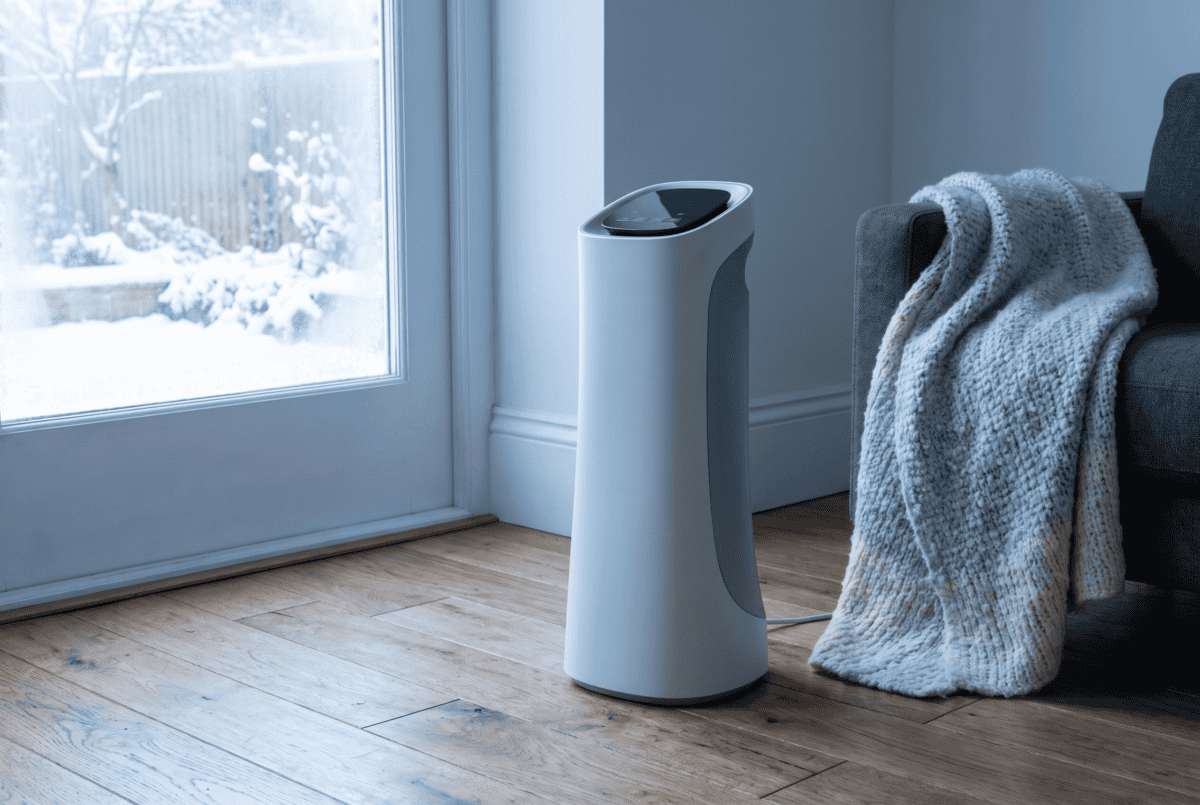 Ceramic tower space heater standing on a wood floor in a chilly living room with snow visible through the window